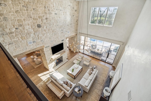 living area featuring wood finished floors, a towering ceiling, and a lit fireplace