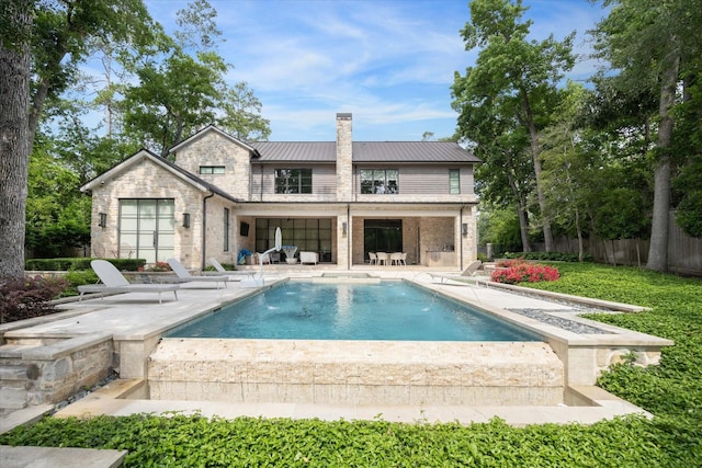 rear view of property featuring fence, a chimney, stone siding, a patio area, and metal roof