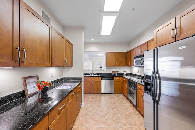 kitchen with a sink, dark stone counters, brown cabinetry, and stainless steel appliances