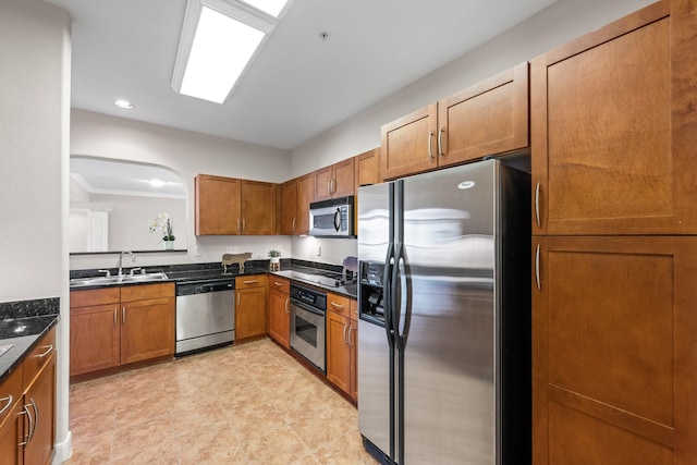 kitchen with dark countertops, stainless steel appliances, brown cabinetry, and a sink