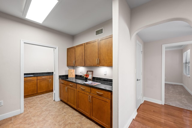 kitchen featuring arched walkways, visible vents, brown cabinetry, and baseboards