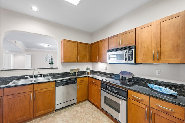 kitchen with a sink, dark stone counters, appliances with stainless steel finishes, and brown cabinetry