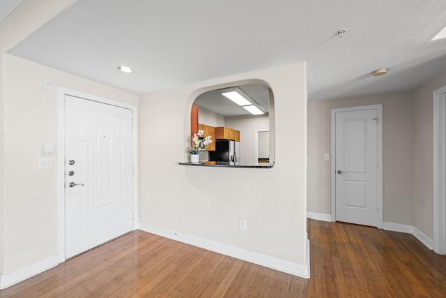 entrance foyer with arched walkways, wood finished floors, baseboards, and a textured ceiling