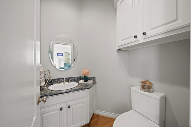 half bathroom with toilet, vanity, baseboards, and wood finished floors