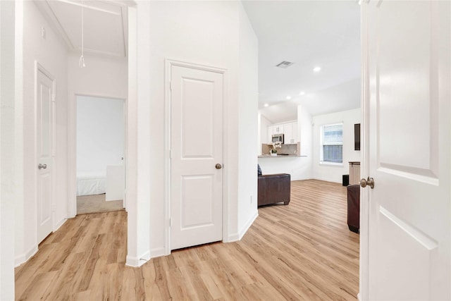 corridor with baseboards, attic access, light wood-style flooring, and vaulted ceiling