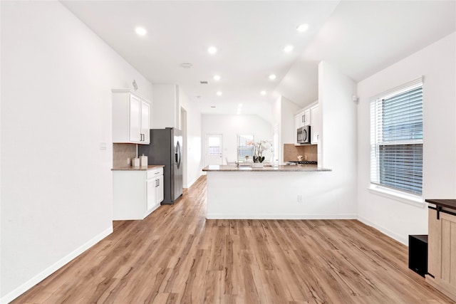 kitchen with white cabinetry, light wood finished floors, backsplash, and stainless steel appliances