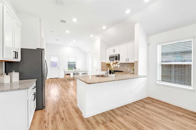 kitchen with stainless steel microwave, a healthy amount of sunlight, white cabinets, and vaulted ceiling