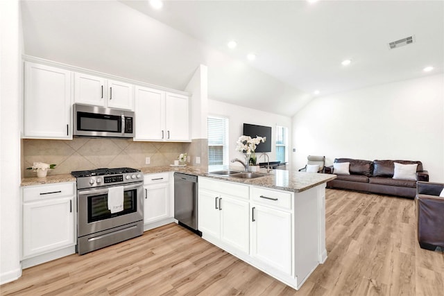 kitchen with visible vents, a peninsula, a sink, vaulted ceiling, and appliances with stainless steel finishes