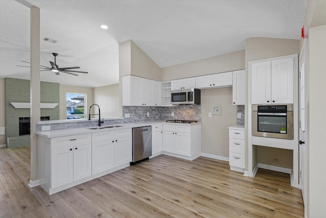 kitchen with lofted ceiling, a peninsula, a sink, light countertops, and appliances with stainless steel finishes