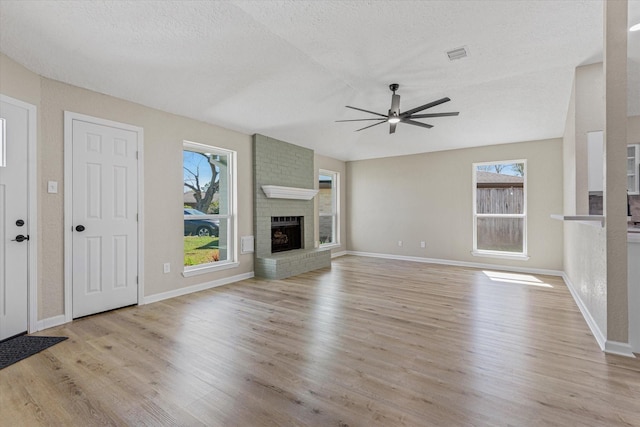 unfurnished living room featuring visible vents, plenty of natural light, a brick fireplace, and light wood-style floors