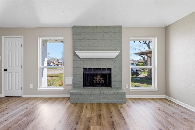 unfurnished living room featuring wood finished floors, plenty of natural light, a fireplace, and baseboards