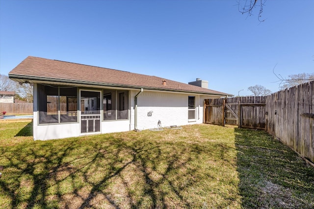 back of property with brick siding, a sunroom, a chimney, a fenced backyard, and a yard