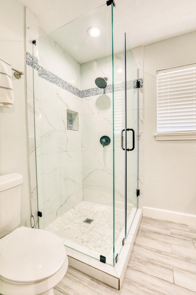 full bath featuring a marble finish shower, toilet, and baseboards