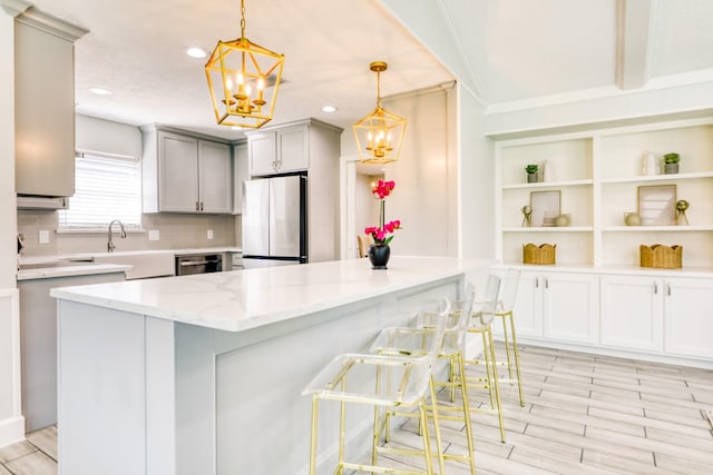 kitchen featuring backsplash, a breakfast bar, light stone counters, gray cabinets, and freestanding refrigerator