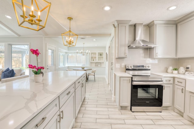 kitchen featuring a notable chandelier, light stone counters, stainless steel range with electric cooktop, wall chimney range hood, and decorative backsplash