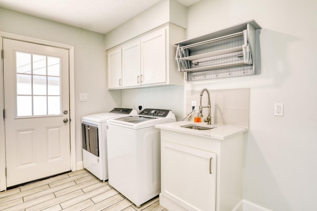 washroom featuring baseboards, light wood finished floors, washing machine and clothes dryer, cabinet space, and a sink