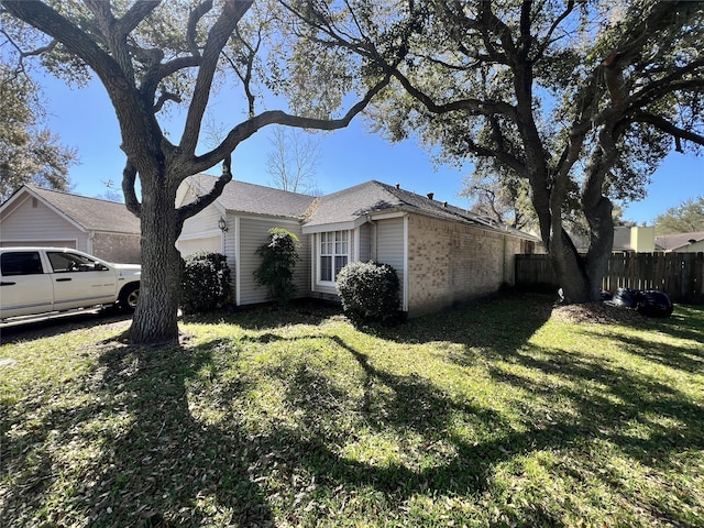 view of side of property featuring a garage, a lawn, brick siding, and fence