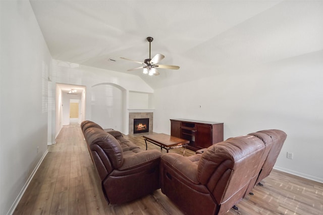 living area featuring a ceiling fan, a tile fireplace, hardwood / wood-style floors, baseboards, and vaulted ceiling