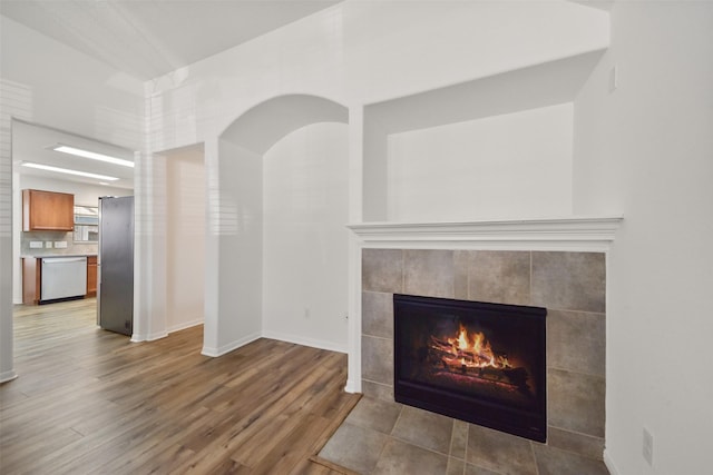 room details with dishwasher, a fireplace, freestanding refrigerator, wood finished floors, and arched walkways