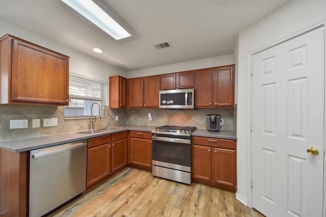 kitchen with light wood finished floors, visible vents, brown cabinets, stainless steel appliances, and a sink