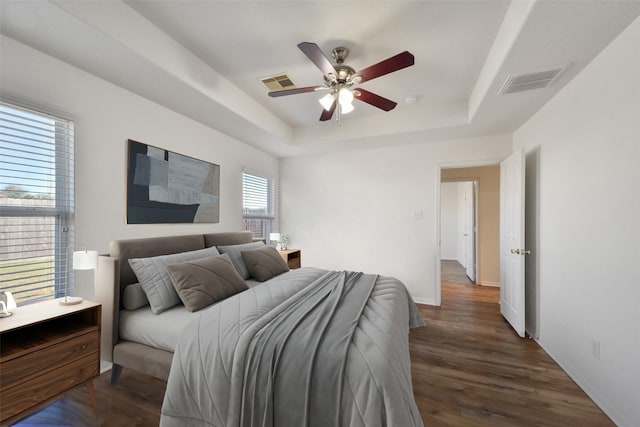 bedroom with a tray ceiling, visible vents, baseboards, and dark wood finished floors