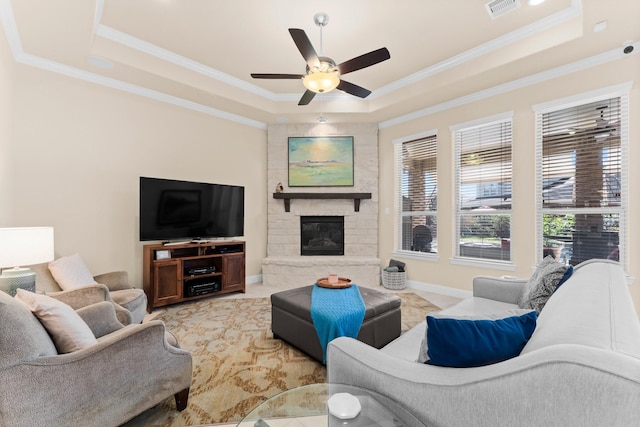 living area with a tray ceiling, visible vents, a fireplace, and crown molding