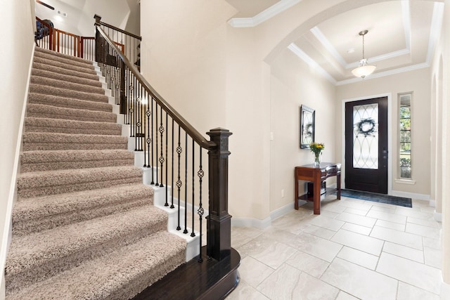 foyer entrance with baseboards, a raised ceiling, ornamental molding, and a towering ceiling