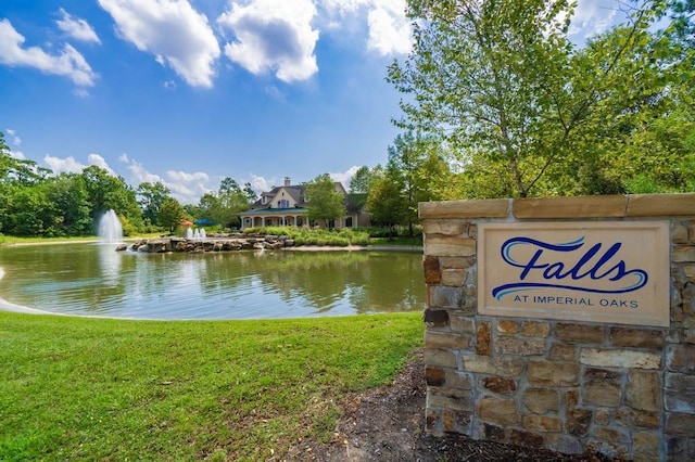 community / neighborhood sign featuring a water view and a lawn