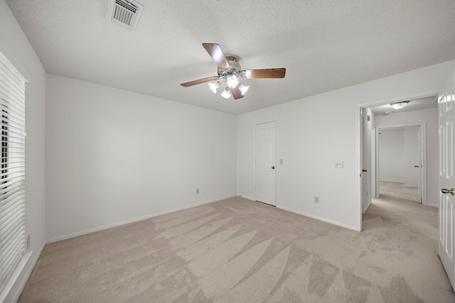 unfurnished bedroom featuring a ceiling fan, baseboards, visible vents, a textured ceiling, and light colored carpet