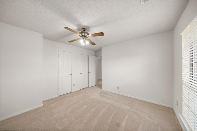 unfurnished bedroom featuring baseboards, ceiling fan, a textured ceiling, light carpet, and two closets