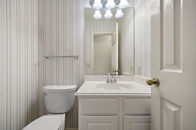 half bath with toilet, vanity, and wallpapered walls