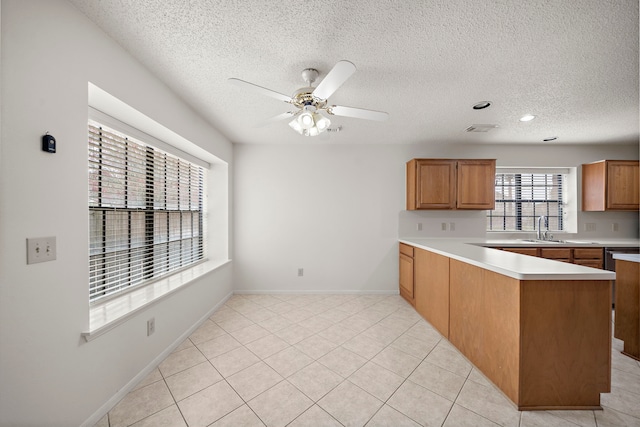 kitchen featuring light tile patterned floors, a ceiling fan, a peninsula, a sink, and light countertops