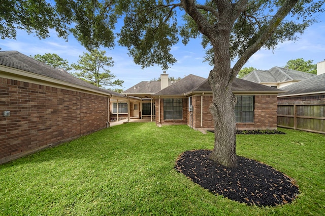 back of property featuring fence, a lawn, brick siding, and a chimney