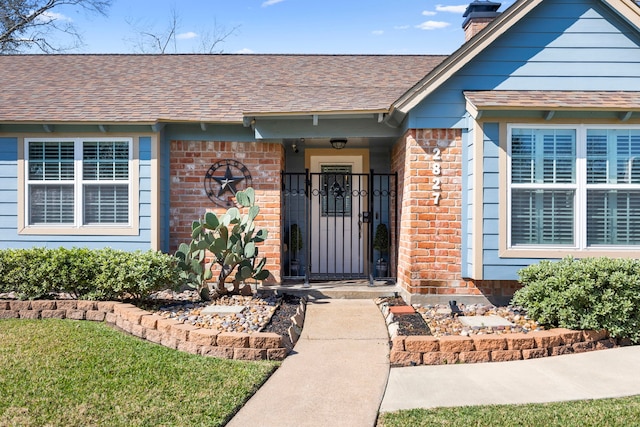 doorway to property with brick siding, roof with shingles, and a chimney