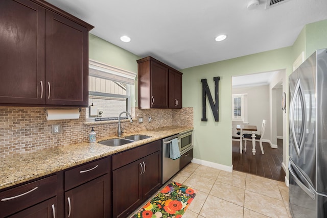 kitchen featuring light stone counters, light tile patterned flooring, a sink, appliances with stainless steel finishes, and backsplash