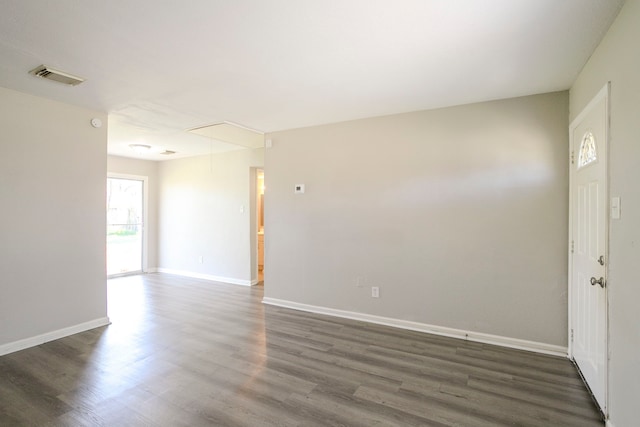 unfurnished room featuring visible vents, attic access, dark wood-type flooring, and baseboards