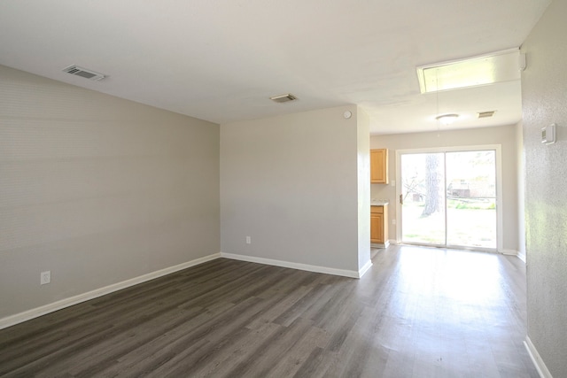 spare room featuring visible vents, attic access, baseboards, and dark wood-style flooring