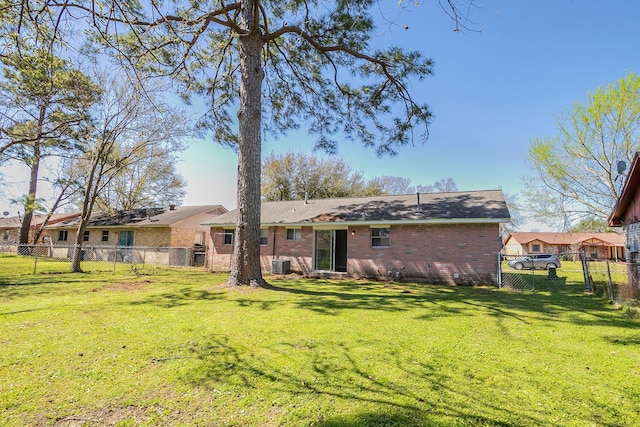 rear view of property featuring a yard, central AC unit, brick siding, and a fenced backyard