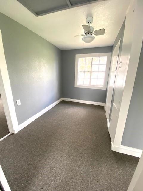 unfurnished room with dark colored carpet, baseboards, attic access, and a ceiling fan