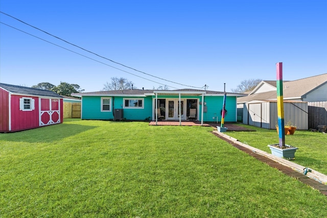 rear view of property featuring fence, an outdoor structure, french doors, a storage shed, and a lawn