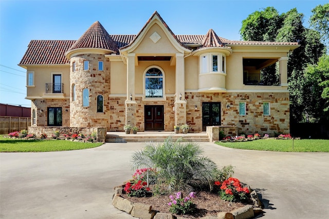 mediterranean / spanish-style home with french doors, stone siding, a balcony, and stucco siding