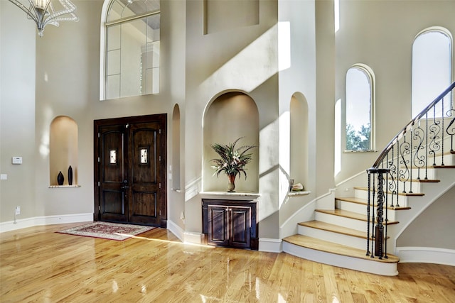 entryway with stairway, baseboards, wood finished floors, and a towering ceiling