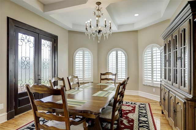 dining area with baseboards, light wood-style flooring, french doors, a raised ceiling, and a notable chandelier