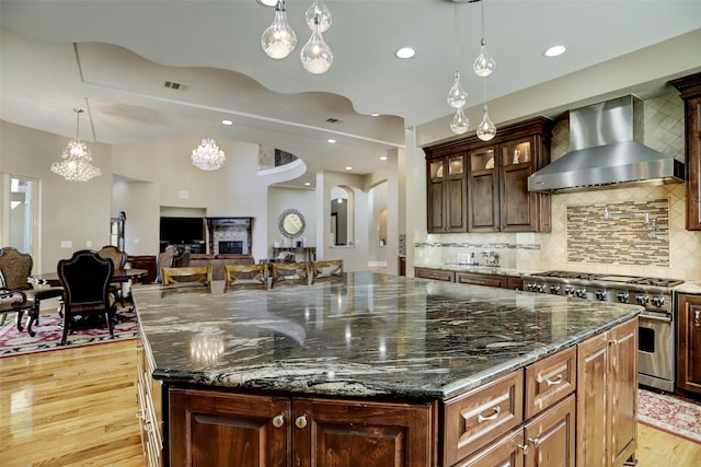 kitchen with visible vents, arched walkways, stainless steel stove, wall chimney exhaust hood, and light wood-type flooring