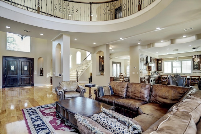 living area featuring light wood-type flooring, visible vents, a towering ceiling, and stairway