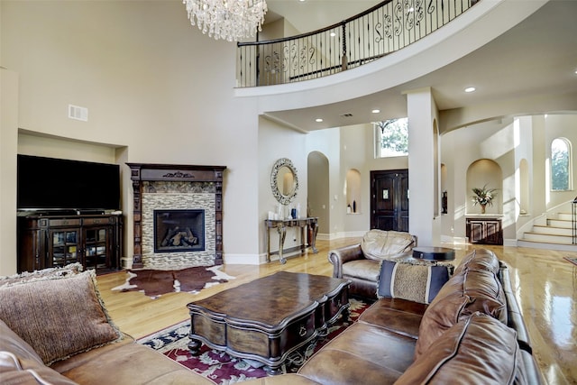 living room featuring visible vents, stairs, a stone fireplace, wood finished floors, and arched walkways