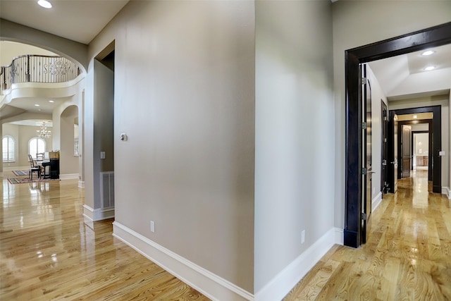 corridor with light wood finished floors, baseboards, recessed lighting, an inviting chandelier, and arched walkways