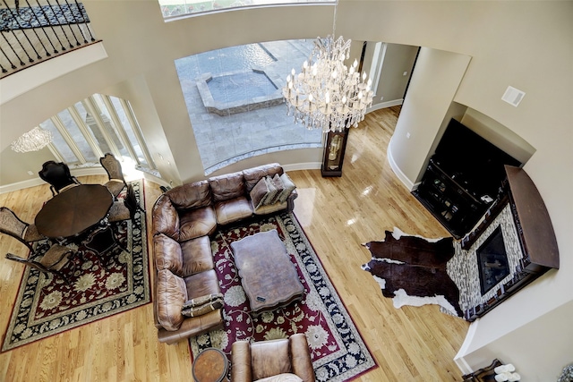 living room featuring wood finished floors, a high ceiling, an inviting chandelier, a fireplace, and baseboards