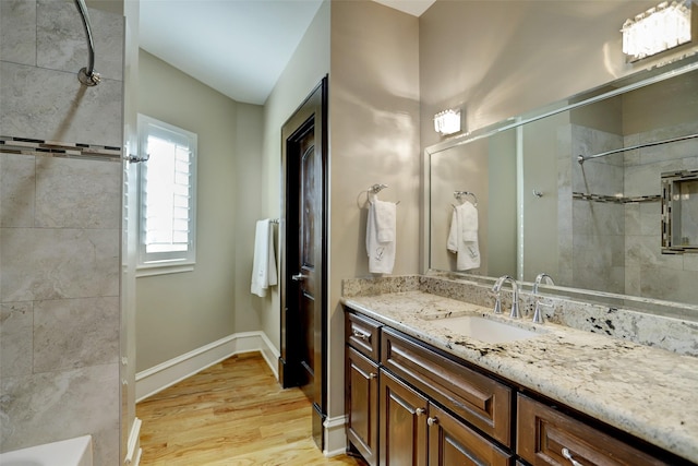 full bath featuring baseboards, wood finished floors, vanity, and a tile shower