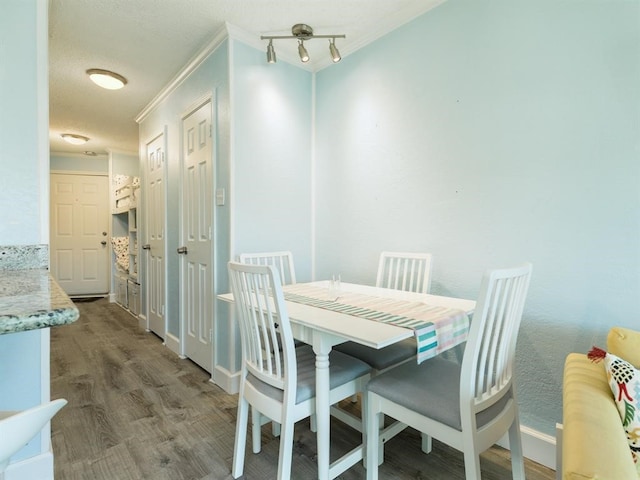 dining space featuring a textured ceiling, wood finished floors, baseboards, and ornamental molding